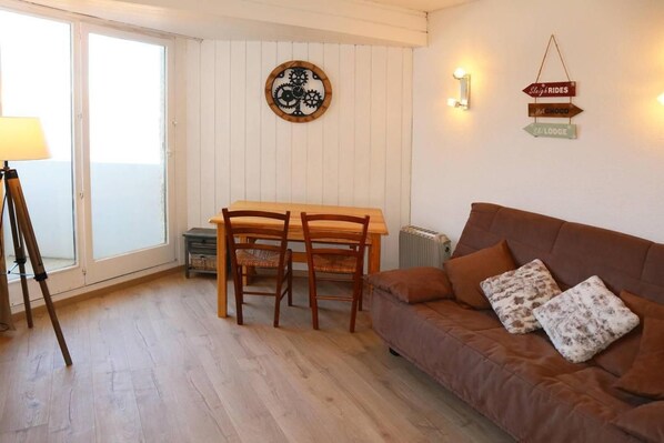 A cozy room with a brown sofa, two wooden chairs, a small table, and a window with blinds.