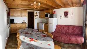 A cozy room with a bed, wooden furniture, a kitchenette, and a red patterned sofa. - 100m from ski slopes, 2nd floor, view ski slopes/mountain, tv, 60m², Les Saisies (Les Saisies)