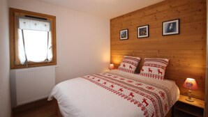 A bedroom with a wooden headboard, a window with curtains, a bed with patterned bedding, and three framed pictures on the wall. - 100m from ski slopes, Ground floor, terrace, tv, ski locker, 47m², Les Saisies (Hauteluce)
