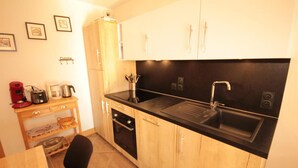 A compact kitchen with wooden cabinets, a black countertop, and a sink. There is a small dining table with chairs, and kitchen appliances like a coffee maker and toaster. - 100m from ski slopes, Ground floor, terrace, tv, ski locker, 47m², Les Saisies (Hauteluce)