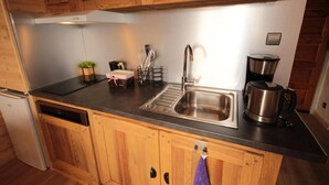 Une cuisine compacte avec des meubles en bois, un évier en acier inoxydable, une machine à café et un égouttoir à vaisselle.