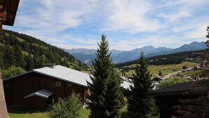 Un chalet de montagne avec un toit en pente, entouré d’une forêt dense et offrant une vue sur les montagnes lointaines.