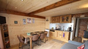 L’intérieur chaleureux d’un chalet avec une table à manger en bois, des chaises, un canapé et un coin cuisine.