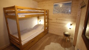 Une chambre avec un lit superposé en bois, un tableau encadré accroché au mur et un petit tabouret.