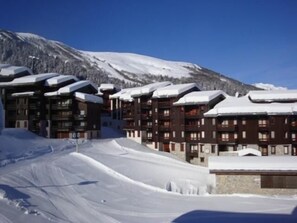 A snow-covered ski resort with multiple buildings, including a lodge with balconies and a ski lift visible in the background.