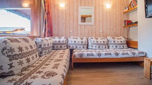Ett mysigt rum med en väggpanel av trä, en soffa med mönstrade kuddar, ett litet bord och en hylla med böcker.