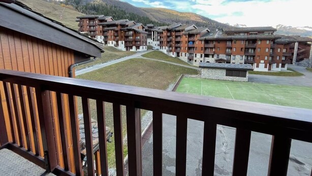 En utsikt från en balkong med utsikt över ett semesterområde med flera byggnader, en gräsyta och berg i bakgrunden.
