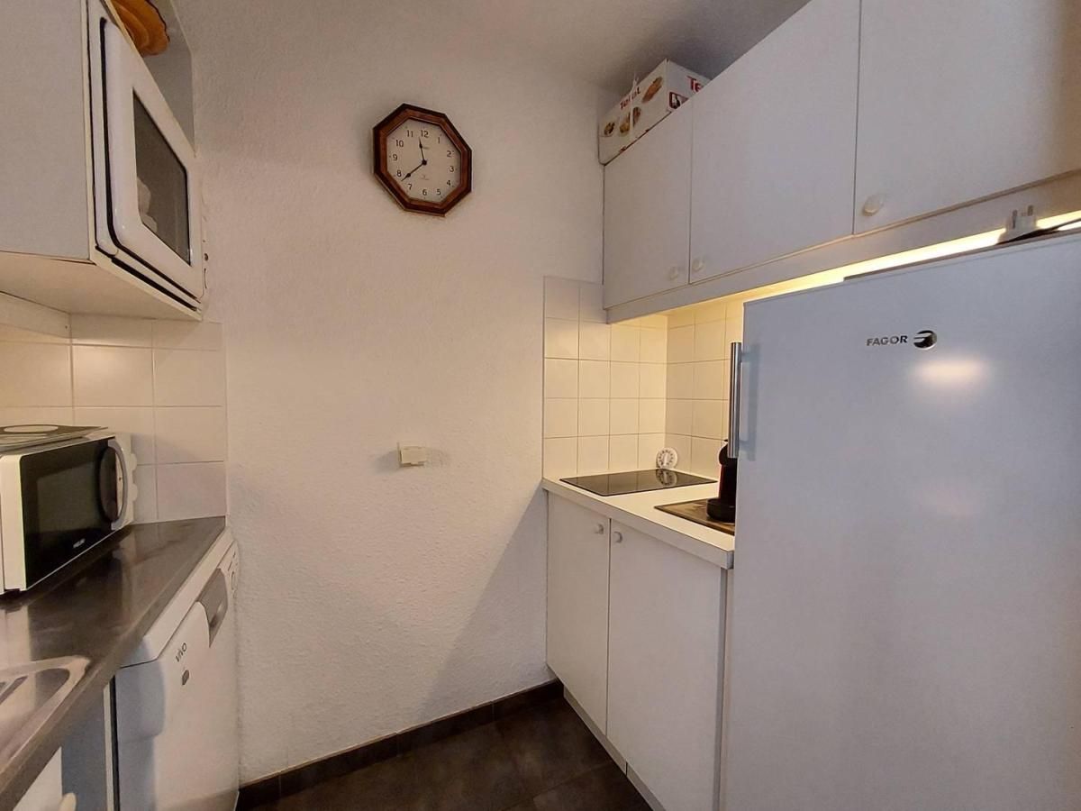 A compact kitchen with a microwave, a refrigerator, and a clock on the wall.