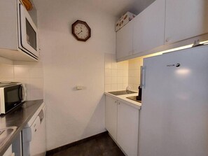A compact kitchen with a microwave, a refrigerator, and a clock on the wall.