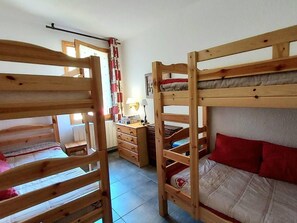 A room with bunk beds, a dresser, a lamp, and a window with curtains.