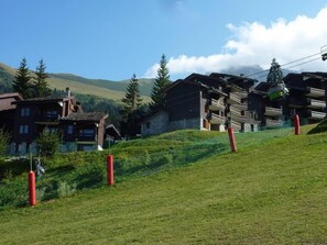 A mountainous area with wooden buildings, a ski lift, and a grassy slope.