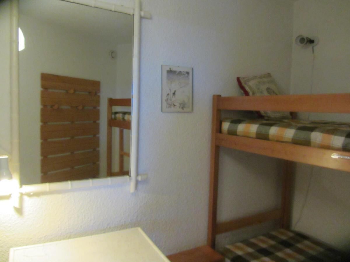 A small, compact room with a bunk bed, a mirror, a framed picture on the wall, and a window with blinds.