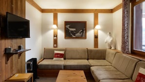 Una sala de estar acogedora con techo de madera, un televisor de pantalla plana, un conjunto de sofás, una mesa de centro y un cuadro enmarcado en la pared.