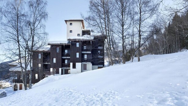 Un edificio moderno de varios pisos con balcones, rodeado de árboles cubiertos de nieve y un cielo despejado.