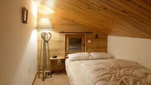 Un dormitorio acogedor en el ático, con techo de madera, lámpara de noche, decoración en forma de corazón y cama con sábanas blancas.