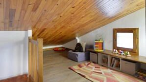 Un dormitorio tipo loft con techo inclinado, una ventana, una estantería y un pequeño rincón de descanso.