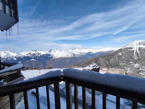 Ein mit Schnee bedeckter Balkon mit Blick auf schneebedeckte Berge und ein Skigebiet im Hintergrund.