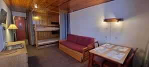 Ein gemütliches Zimmer mit einem Etagenbett, einem roten Schlafsofa, einem Holztisch mit Unterlagen und einer Lampe.