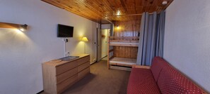 Ein Zimmer mit einem Etagenbett, einer Holzkommode, einem Flachbildfernseher an der Wand und einer Lampe.