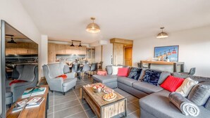 A modern living room with a grey sofa, a wooden coffee table, and a dining area with a kitchen in the background. - 50m from ski slopes, 6th floor, swimming pool, sauna, hammam, balcony, tv, ski locker, 127m², Tignes (Tignes)