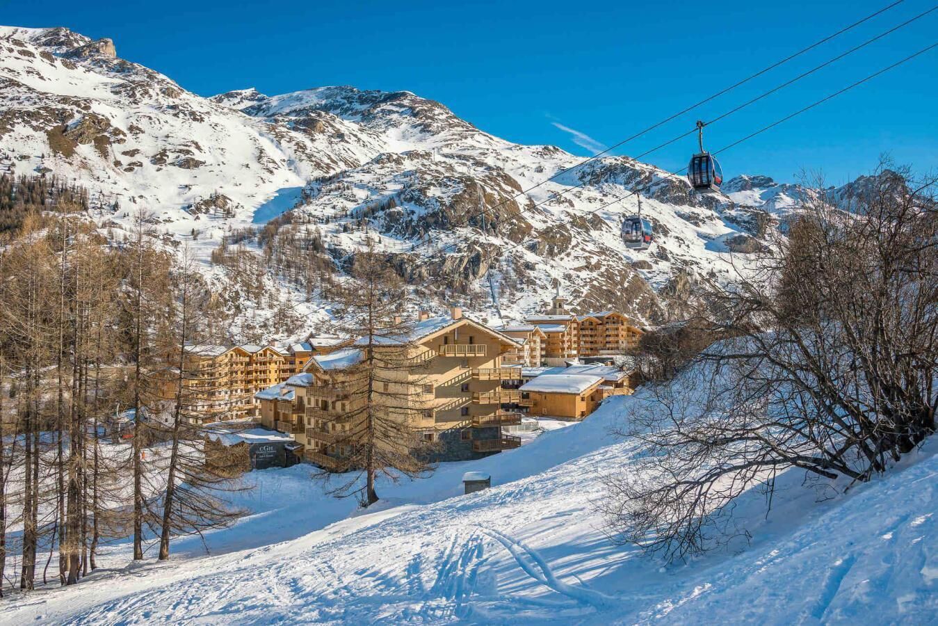 A snow-covered mountain with a ski lift and a cluster of wooden buildings with balconies, likely a ski resort.