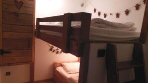 Asuntolatyylinen huone, jossa on kerrossängyt, puinen vaatekaappi ja pieni tikapuut.