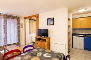A compact room with a dining table, chairs, a television, a small kitchen area, and a bed. - 100m from resort center, Ground floor, swimming pool, sauna, balcony, tv, ski locker, 33m² (Les Orres)