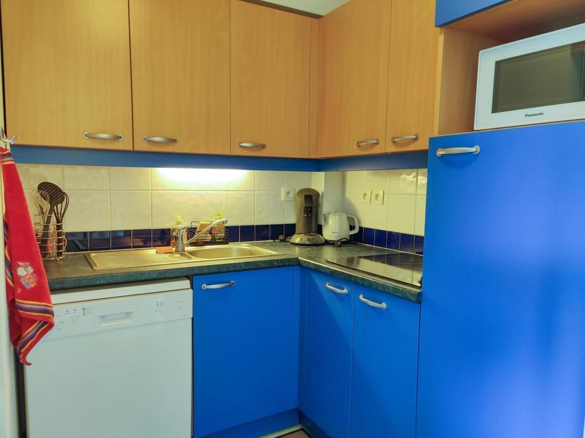 Een compacte keuken met houten bovenkastjes, een blauwe onderkast, een witte vaatwasser en een magnetron bovenop een blauwe koelkast.