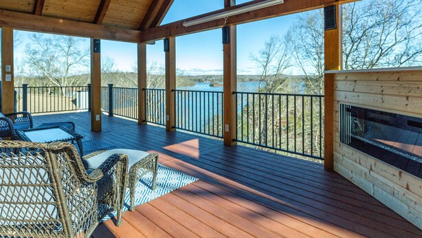 A covered deck with a view of a lake, wooden furniture, and a fireplace. - The View on Lake Lanier lake view & dock. (Gainesville)