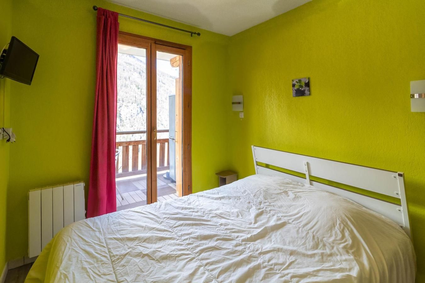 Una camera da letto con un letto, una finestra con tende, un comodino e un punto luce a parete.