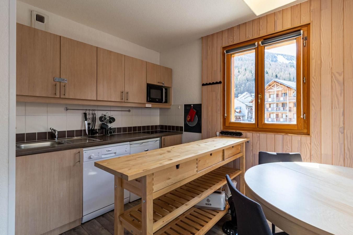 A compact kitchen with wooden cabinets, a built-in microwave, and a window overlooking a mountainous landscape.