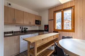 A compact kitchen with wooden cabinets, a built-in microwave, and a window overlooking a mountainous landscape.