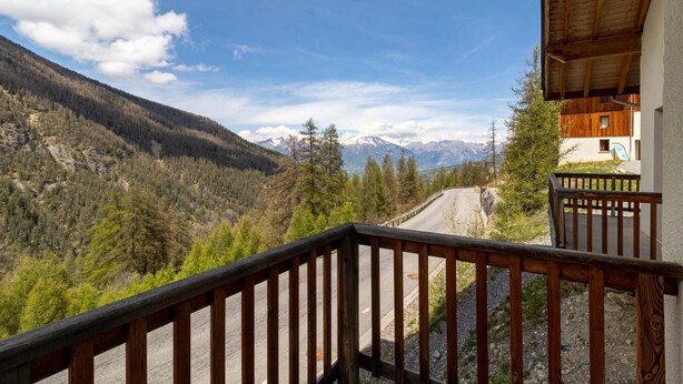 A balcony with a view of a mountain road and forested valley.