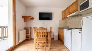 A compact kitchen with wooden cabinets, a built-in microwave, a dishwasher, and a TV mounted on the wall.