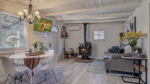 A modern living room with a fireplace, a dining area with a round table and chairs, and a cozy seating area with a sofa and a TV displaying deer. - Cozy Cottage Getaway  (Payson)