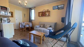 Uma sala de estar acolhedora com um sofá, uma mesa de jantar com cadeiras, um espaço para café e uma cadeira dobrável azul.