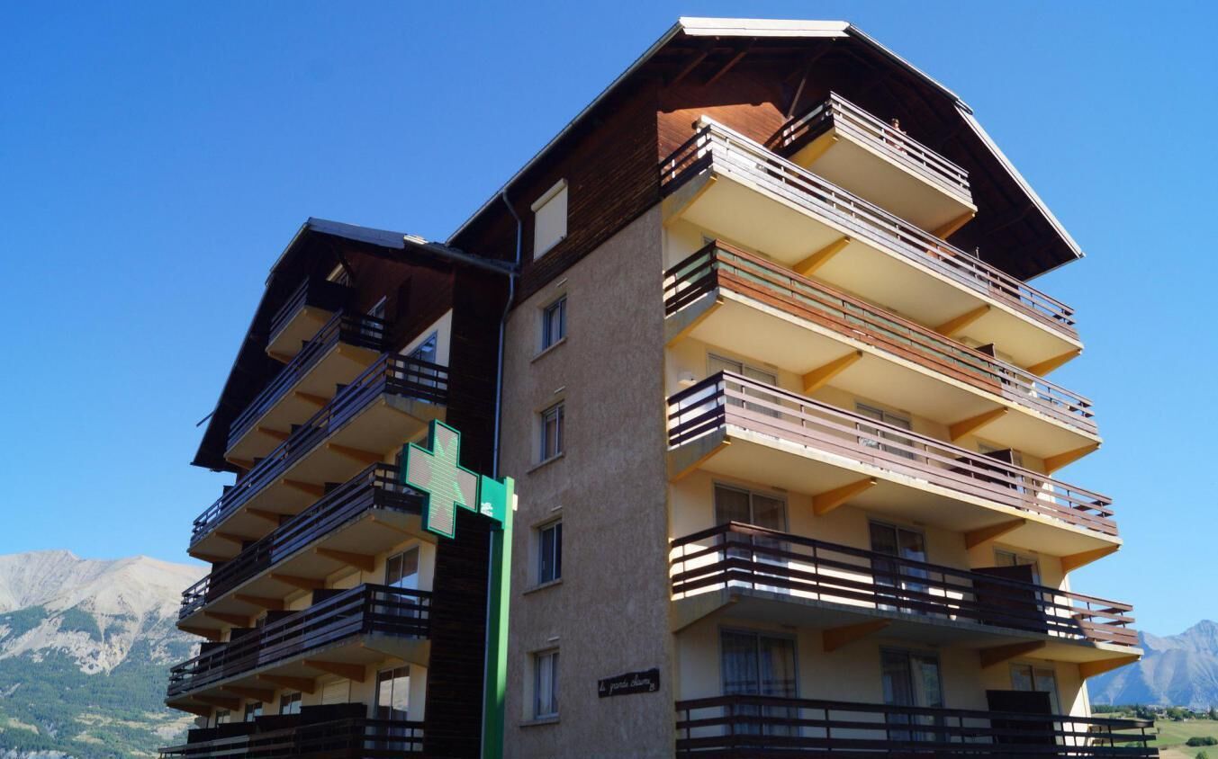 A multi-story hotel with balconies and a mountain backdrop.