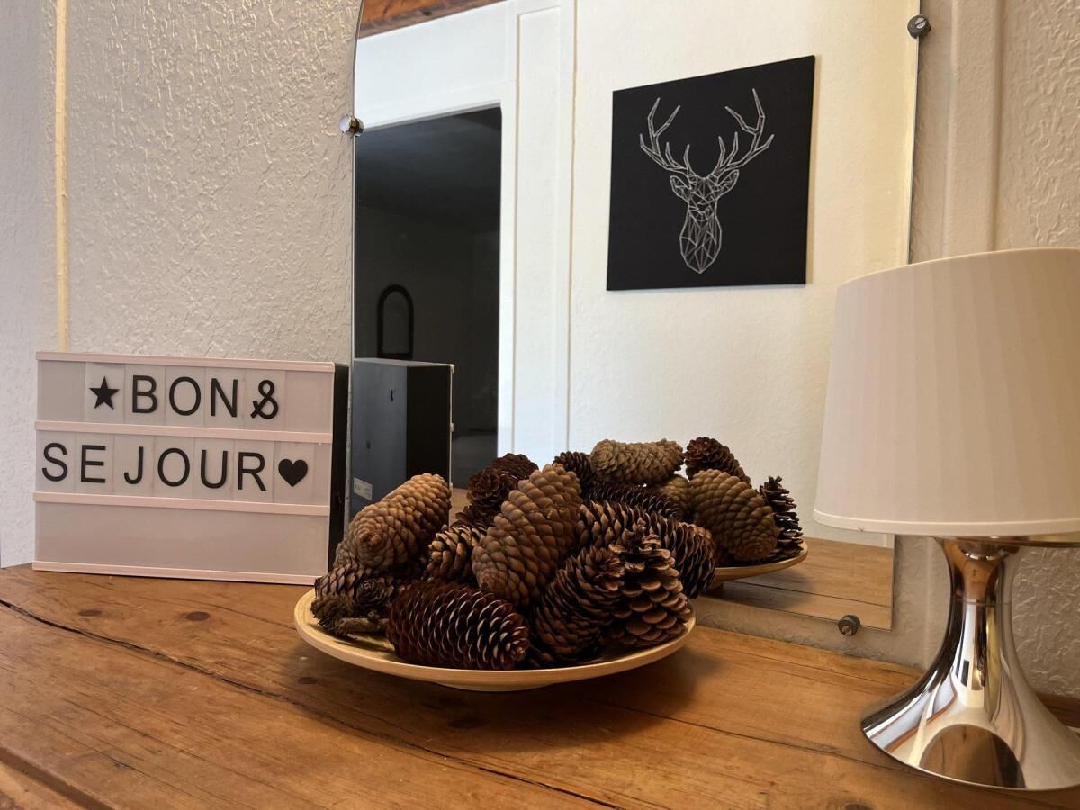 Ein Holztisch mit einer Schale Kiefernzapfen, einem Schild mit der Aufschrift 'BON SE JOUR' und einem Hirschgeweih-Kunstwerk an der Wand.