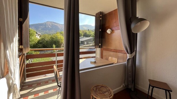Uma varanda com vista para montanhas, uma mesa de madeira, uma cadeira e um banquinho.