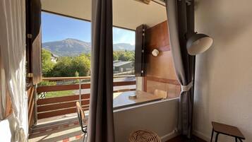Un balcon avec vue sur les montagnes, une table en bois, une chaise et un petit tabouret.