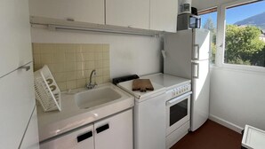 Uma cozinha compacta com pia, fogão e forno, uma pequena janela e vista para o verde lá fora.