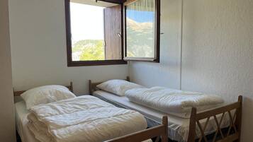 Une chambre avec deux lits simples, une fenêtre donnant sur les montagnes et une tête de lit en bois.