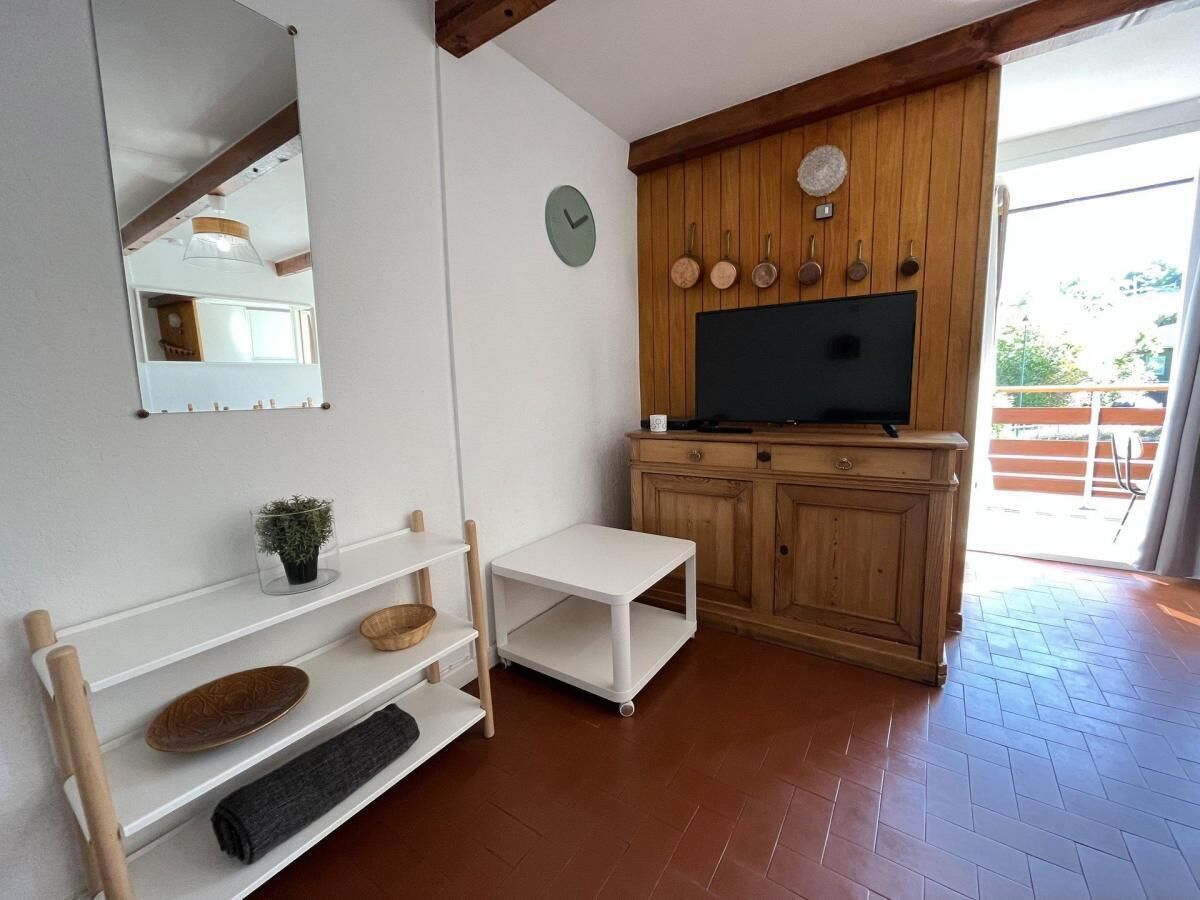 A room with a wooden cabinet, a television, a small table, and shelves with decorative items.