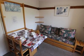 A cozy room with a wooden dining table set for four, a floral sofa, and a small wooden stool.