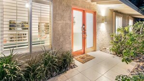 A modern house with a glass door, a tiled patio, and a small garden.
