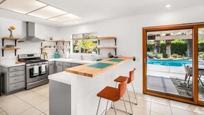 A modern kitchen with a central island, built-in oven, and a view of a swimming pool through a glass door.