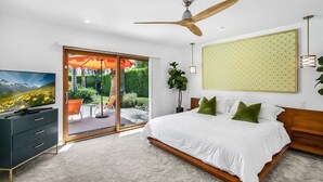 A bedroom with a bed, a TV, a ceiling fan, and a view of a garden through a sliding door.