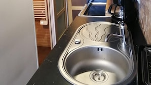 Cocina compacta con un lavamanos de acero inoxidable, una cafetera y un estante de madera.
