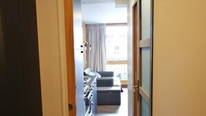 Un pasillo estrecho que conduce a un dormitorio con cama, cómoda y ventana con cortinas.