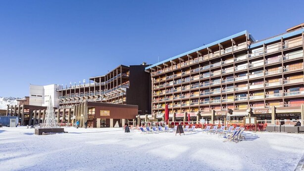 Un hotel con varios balcones, un patio central con una fuente cubierta de nieve y un cielo azul despejado.